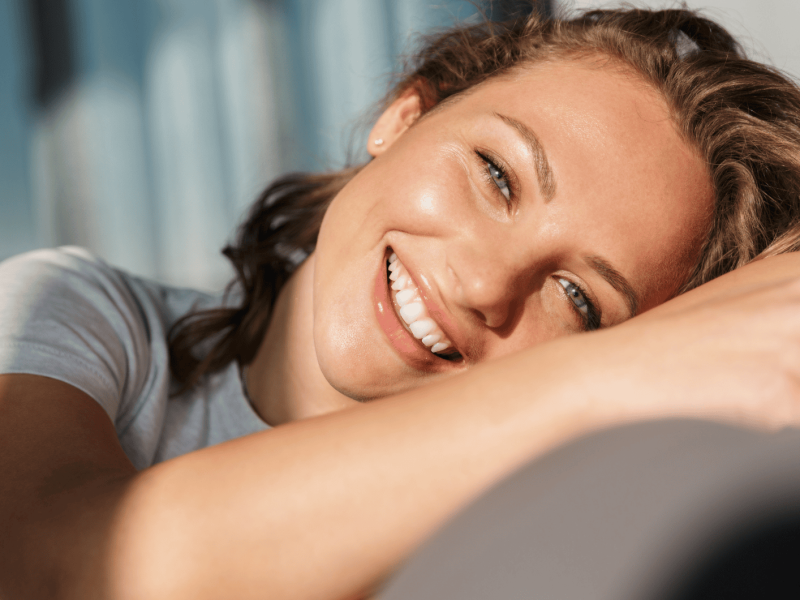 Frau liegt im Sonnenlicht lächelnd auf einem Sofa