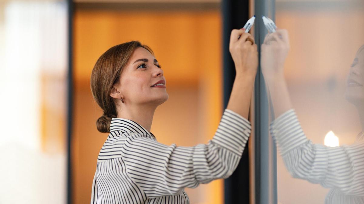 Frau schreibt mit einem Stift auf eine Tafel.