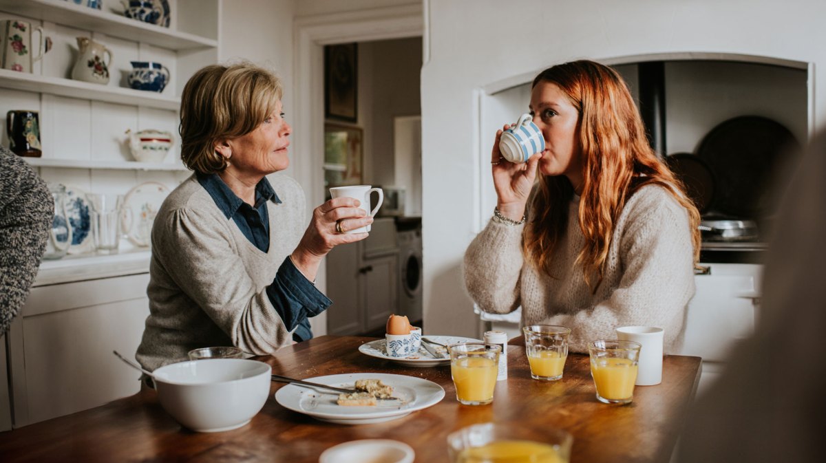 Erwachsene Tochter und Mutter sitzen am Frühstückstisch und unterhalten sich.