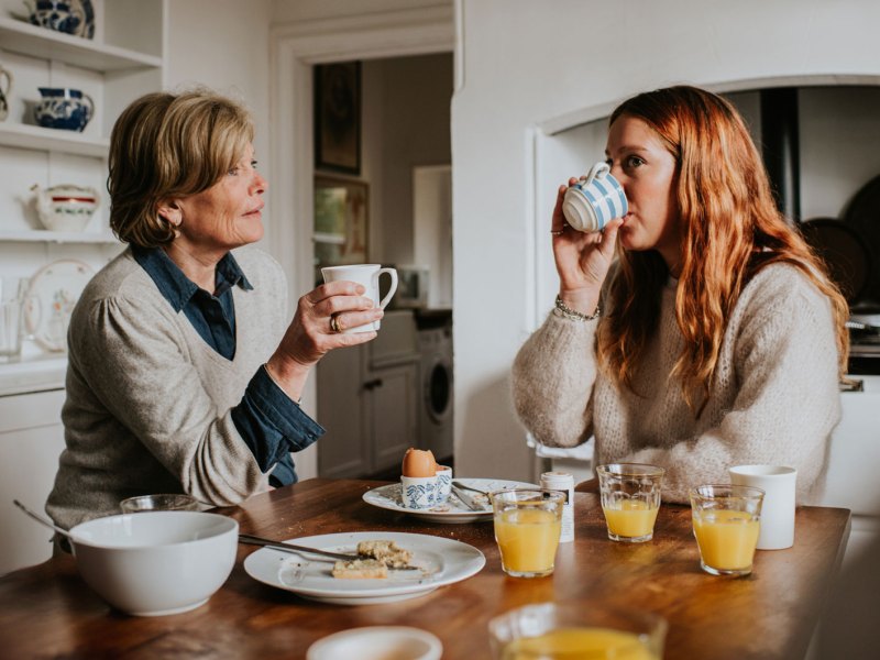Erwachsene Tochter und Mutter sitzen am Frühstückstisch und unterhalten sich.