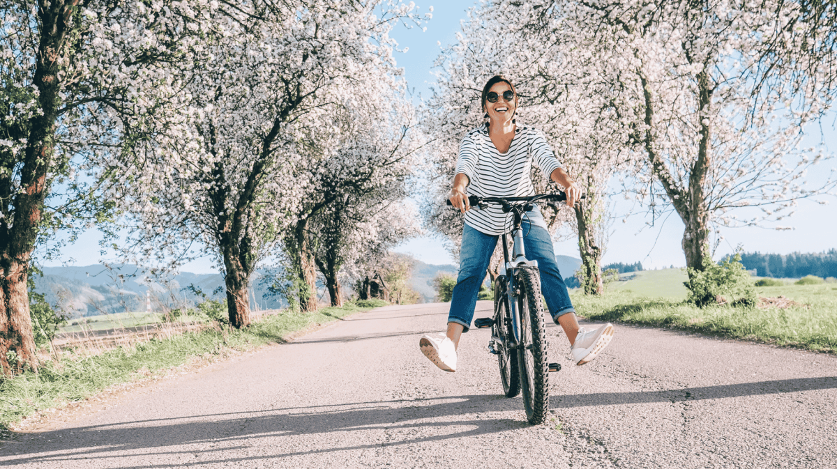 Frau strahlend auf dme Fahrrad umgeben von einer Kirschblütenbaumallee