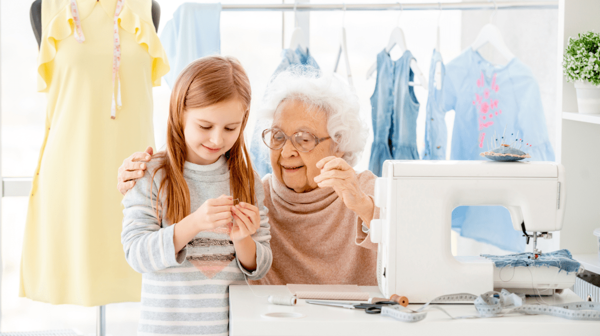 Uroma und Enkeltochter sitzen vor einer Nähmaschine und nähen