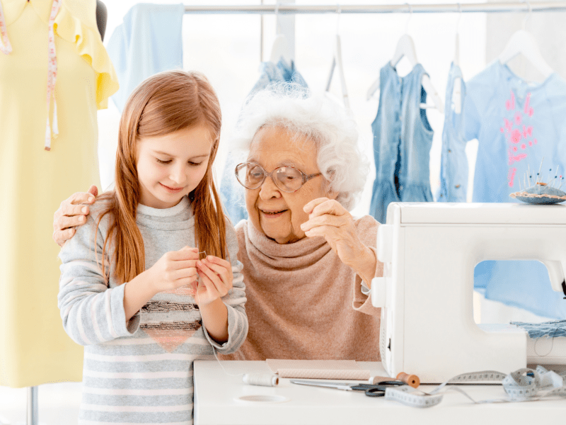 Uroma und Enkeltochter sitzen vor einer Nähmaschine und nähen