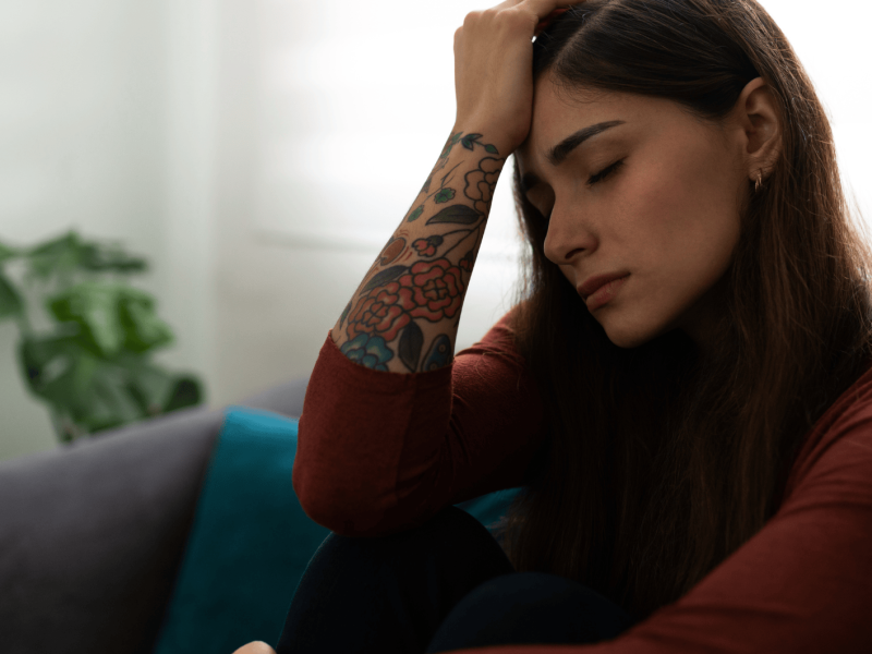 Frau mit Tattoos am Arm sitzt traurig auf einem Sofa