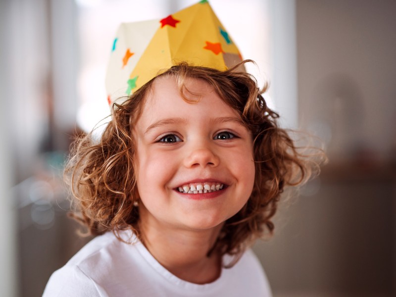 Kleines Kind, ca. 5 Jahre alt, strahlt in die Kamera und trägt eine Krone aus Papier.