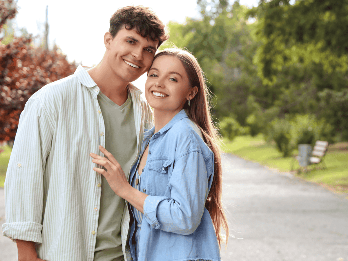Frau und Mann in der Natur umarmen sich seitlich und schauen l&auml;chelnd in die Kamera