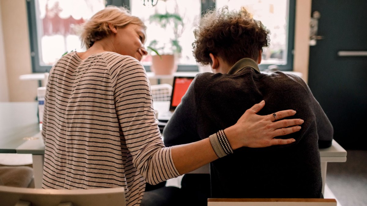 Mutter sitzt neben ihrem Teenager zu Hause und streichelt ihm den Rücken.