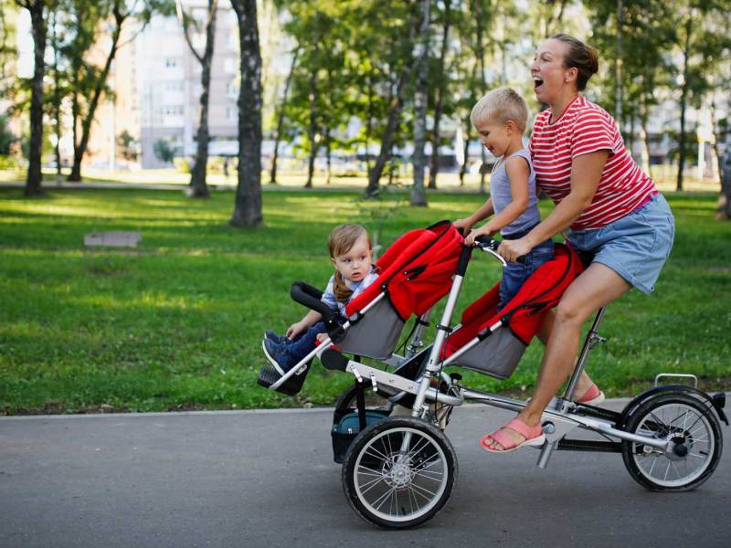 Mutter fährt mit ihren beiden kleinen Kindern auf einer Art Lastenrad durch den Park.