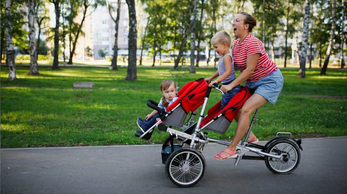 Mutter fährt mit ihren beiden kleinen Kindern auf einer Art Lastenrad durch den Park.