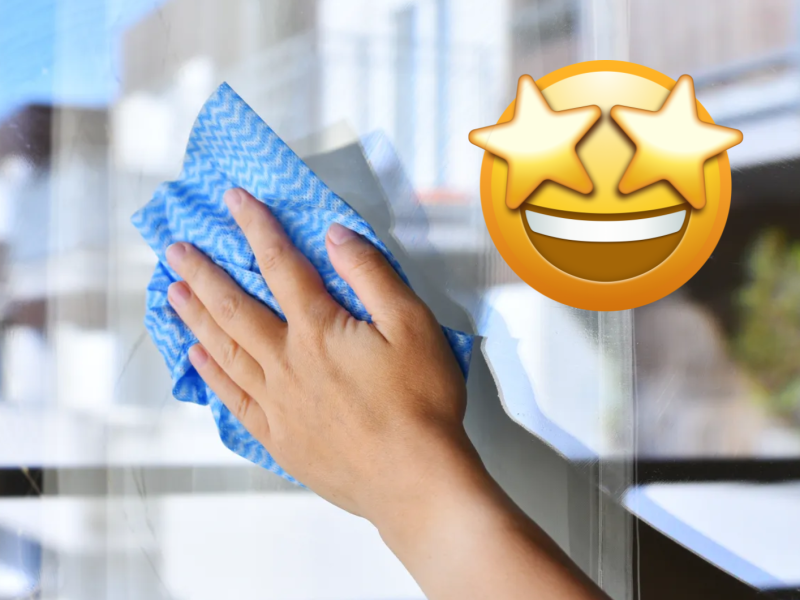Hand mit blauem Lappen putzt Fenster, daneben Emoji