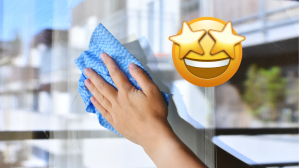 Hand mit blauem Lappen putzt Fenster, daneben Emoji