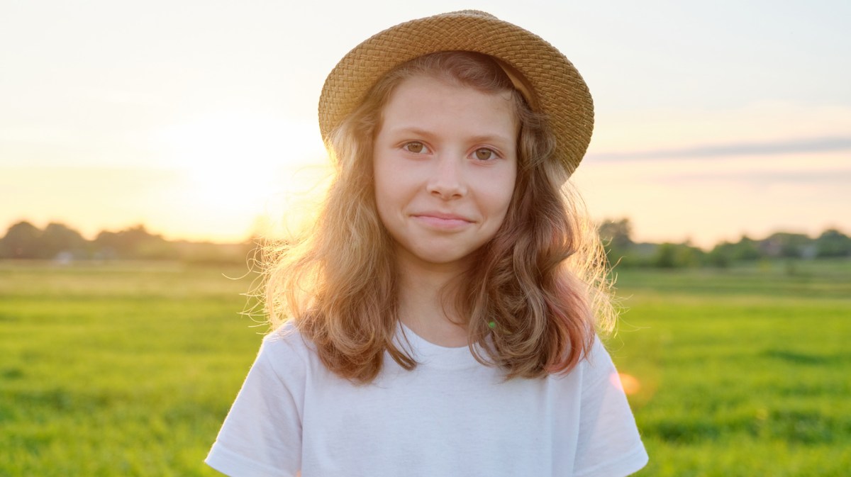 Mädchen, ca. 10 Jahre alt, an einem Sommerabend auf einer weitläufigen Wiese.