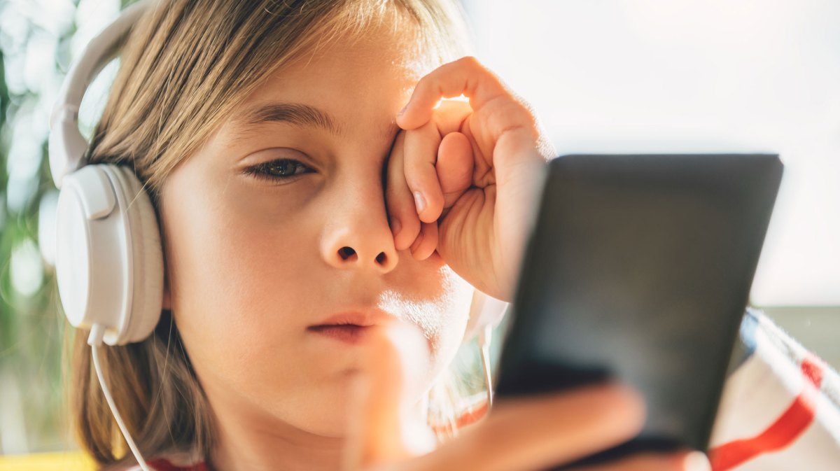 Müdes Mädchen mit Kopfhörern, das auf sein Handy schaut.