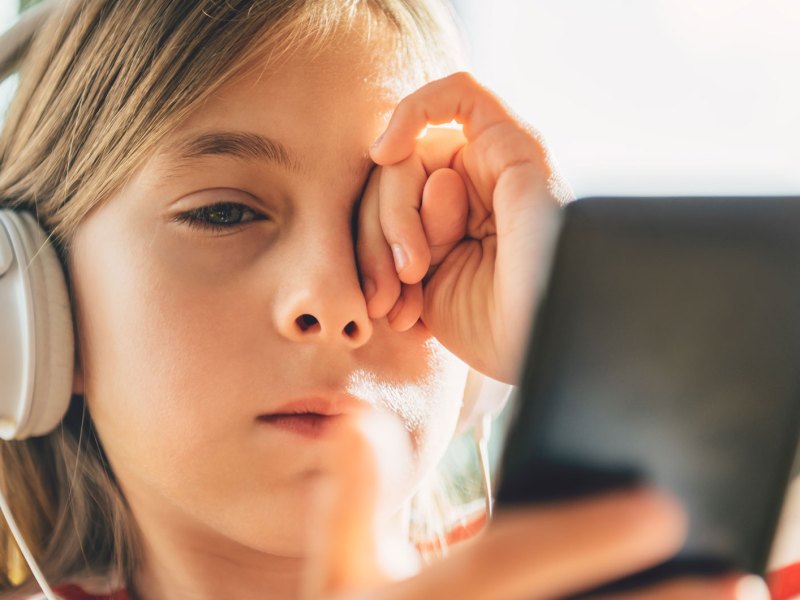 Müdes Mädchen mit Kopfhörern, das auf sein Handy schaut.