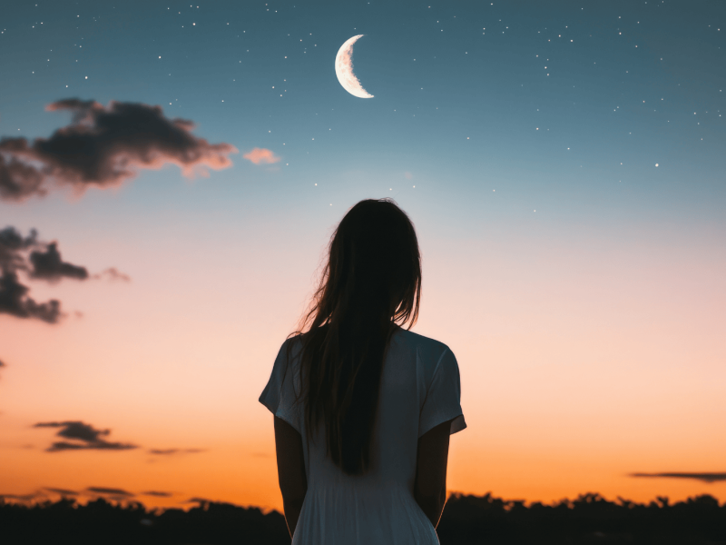 Rötlicher Himmel mit Mondsichel, eine Frau schaut hinauf.