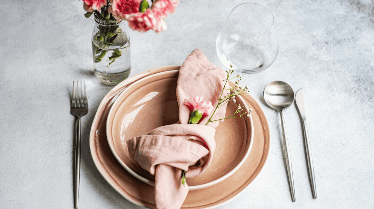 Rosa Geschirr auf grauem Tisch, mit rosa Serviette.