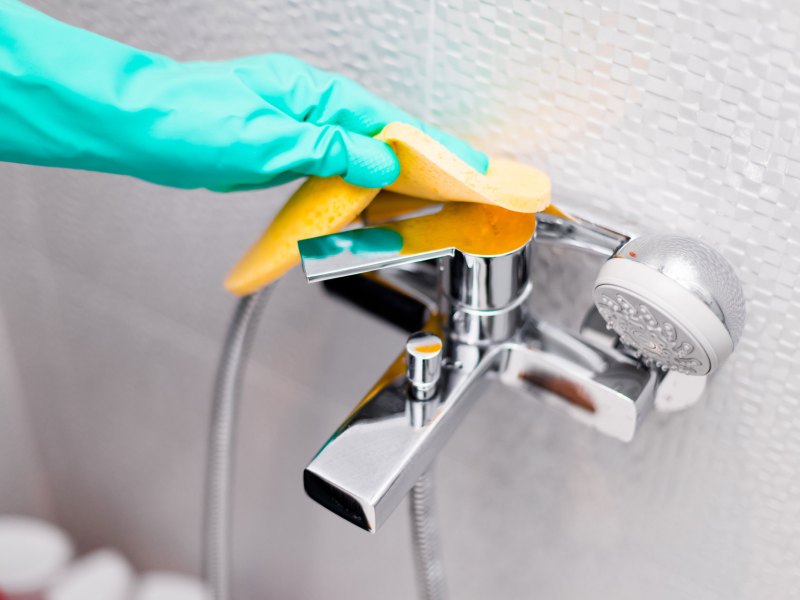 Hand mit Putzhandschuhen in Türkis reinigt Armatur
