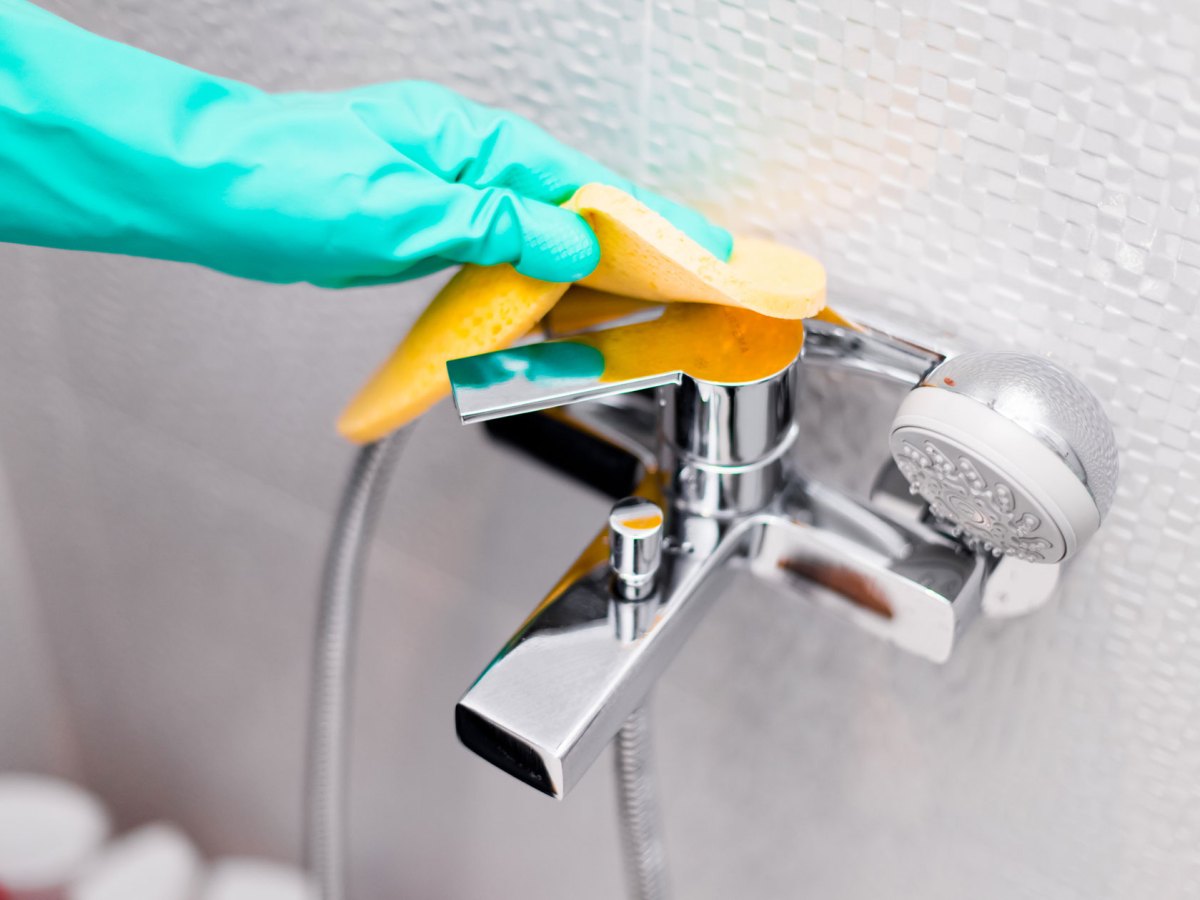 Hand mit Putzhandschuhen in Türkis reinigt Armatur