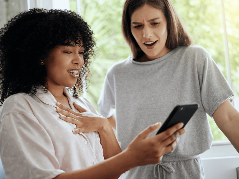 Zwei junge Frauen schauen schockiert auf ein Handy.
