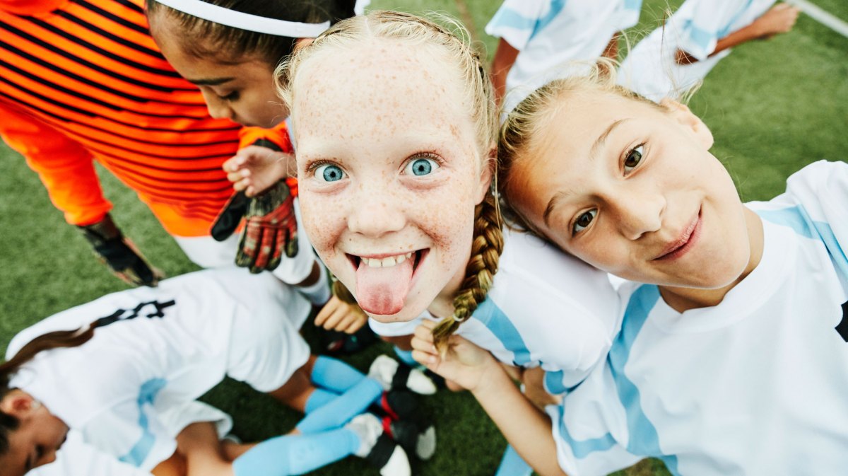 Junge Fußballspielerin streckt die Zunge heraus und albert mit ihren Mitspielerinnen rum.