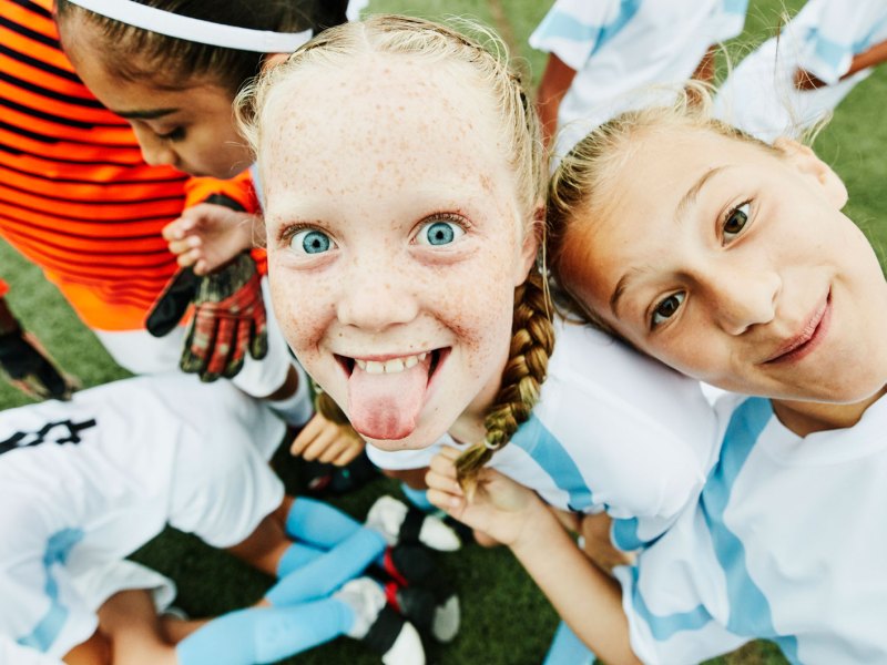 Junge Fußballspielerin streckt die Zunge heraus und albert mit ihren Mitspielerinnen rum.