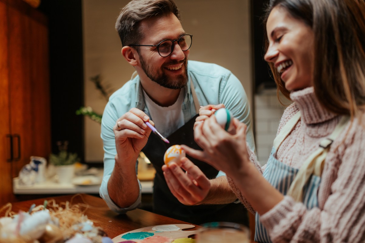 Mann und Frau bemalen Ostereier und lachen gemeinsam