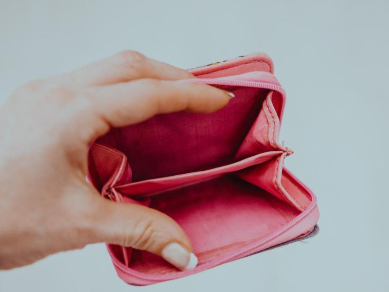 Die Hand einer jungen Frau mit Gelnägeln hält ein leeres Portemonnaie offen in die Kamera.