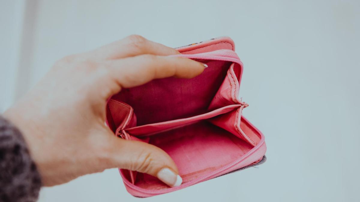 Die Hand einer jungen Frau mit Gelnägeln hält ein leeres Portemonnaie offen in die Kamera.