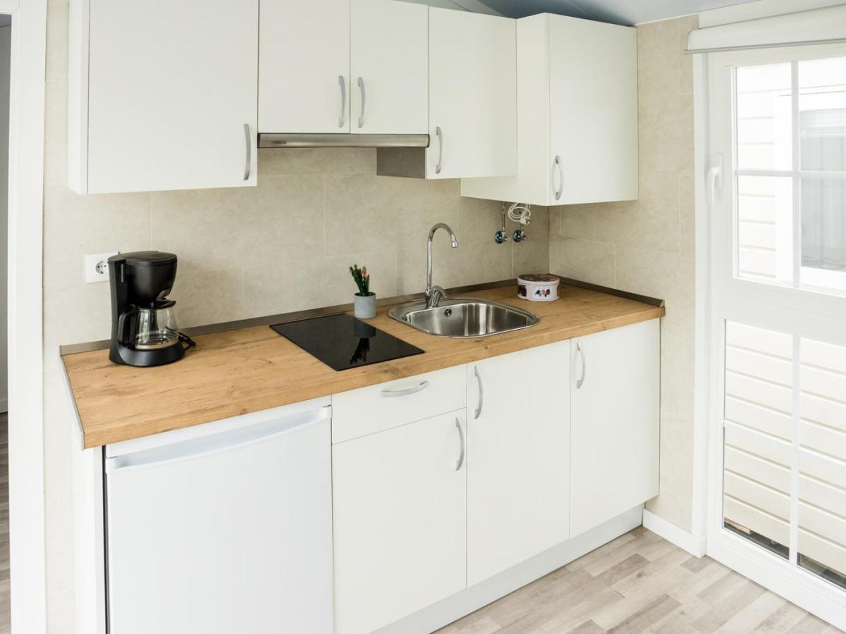 Helle Einbauk&uuml;che mit Holzarbeitsplatte, Kaffeemaschine, Sp&uuml;le und Glaskeramikfeld vor gro&szlig;em Fenster.