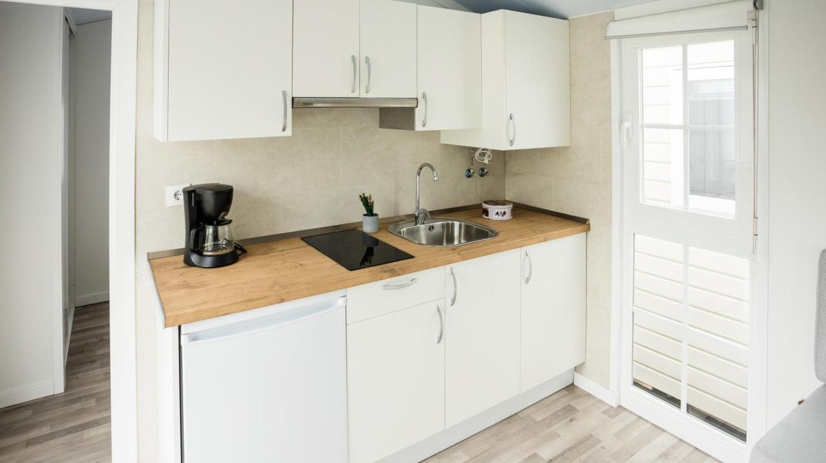 Helle Einbauküche mit Holzarbeitsplatte, Kaffeemaschine, Spüle und Glaskeramikfeld vor großem Fenster.