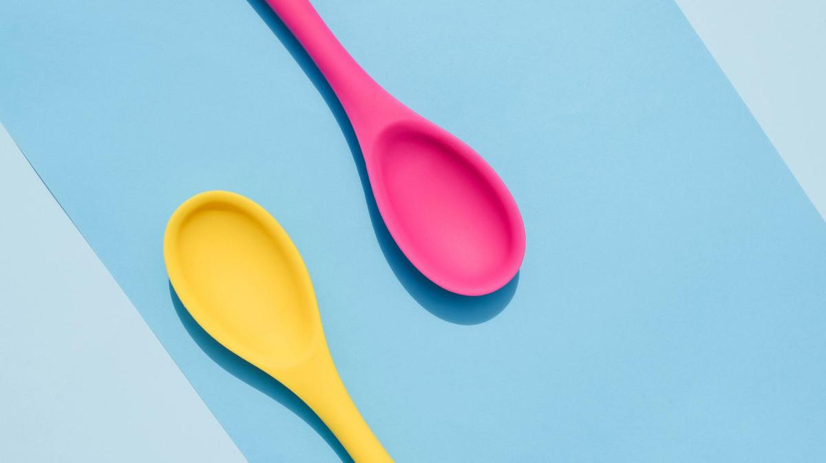 ein pinker und ein gelber Plastiklöffel liegen auf einer blauen Unterlage.