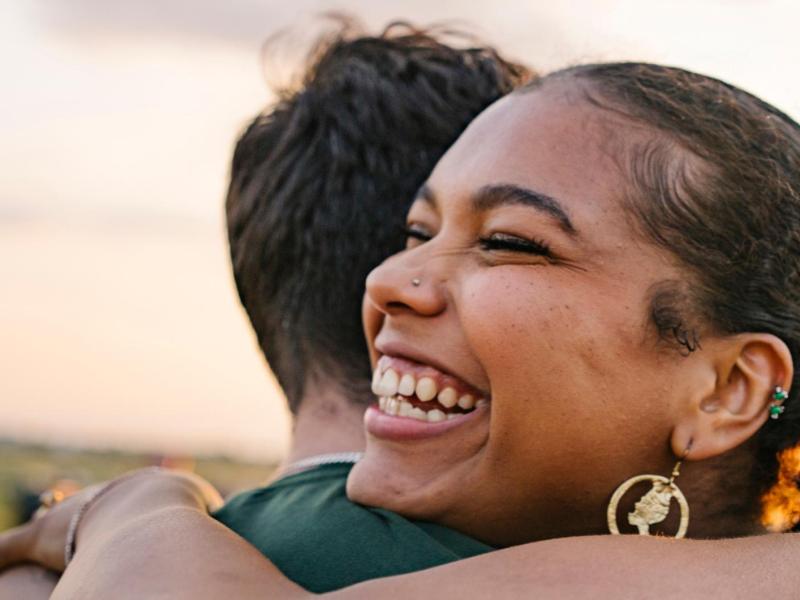 Junge Frau mit schwarzen Haaren und Nasenpiercng umarmt ihren Partner.