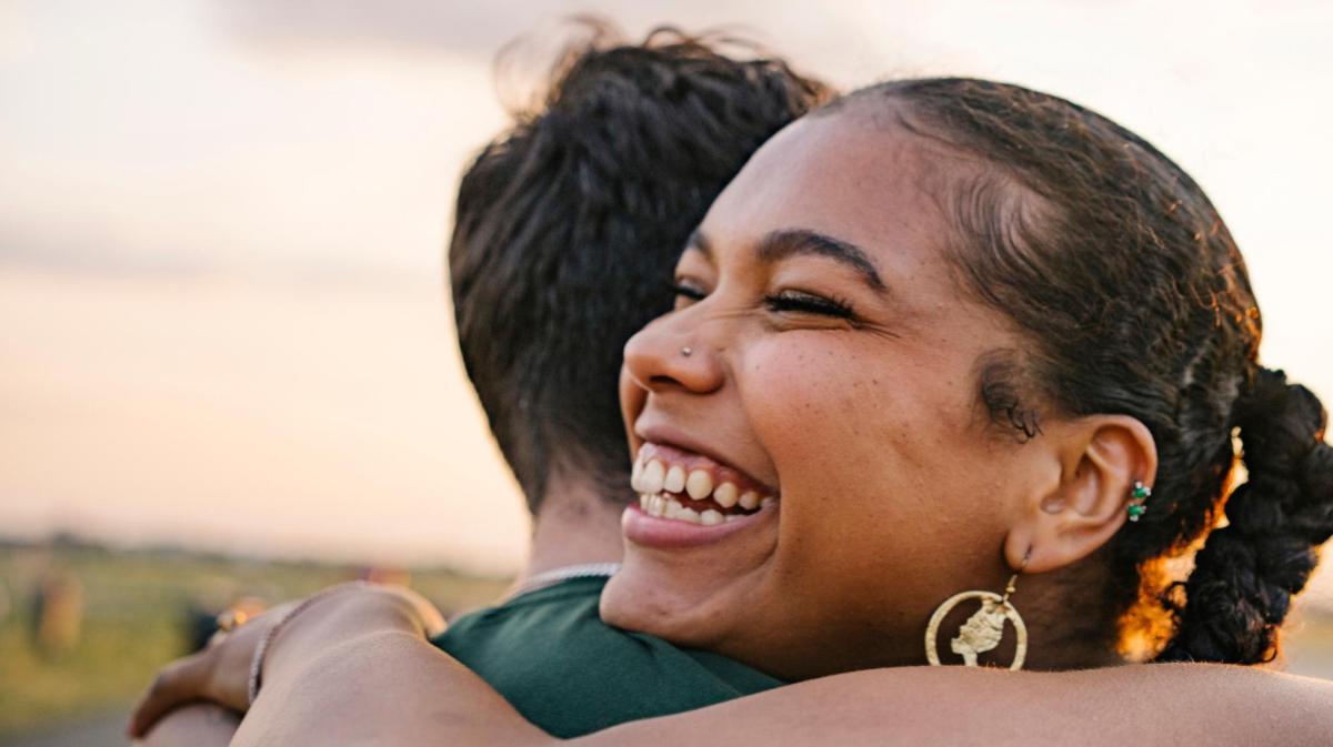Junge Frau mit schwarzen Haaren und Nasenpiercng umarmt ihren Partner.