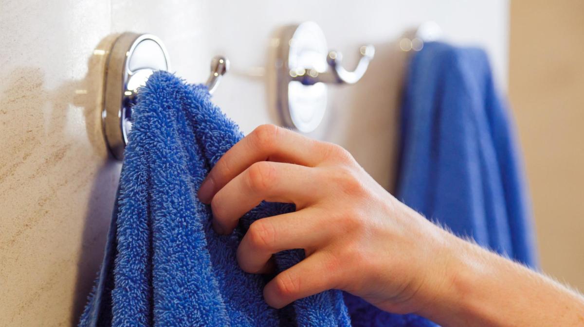 Frau nimmt ein blaues Dusschhandtuch vom Haken.