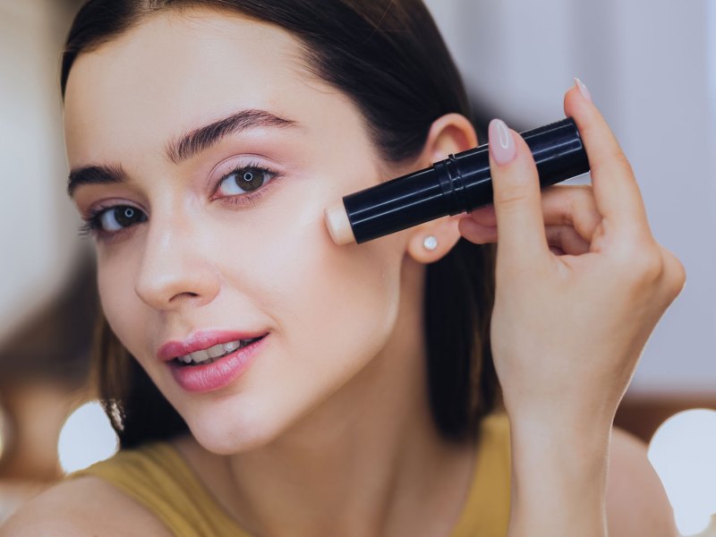 Frau, die mit einem Stift Make-up auftr&auml;gt.