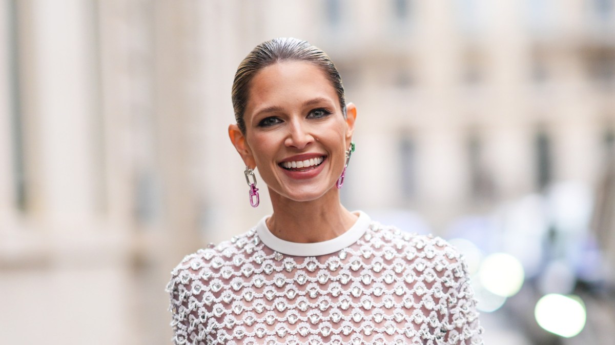 Frau mit einem Designer-Kleid und schicken Ohrringen, die in die Kamera lächelt.