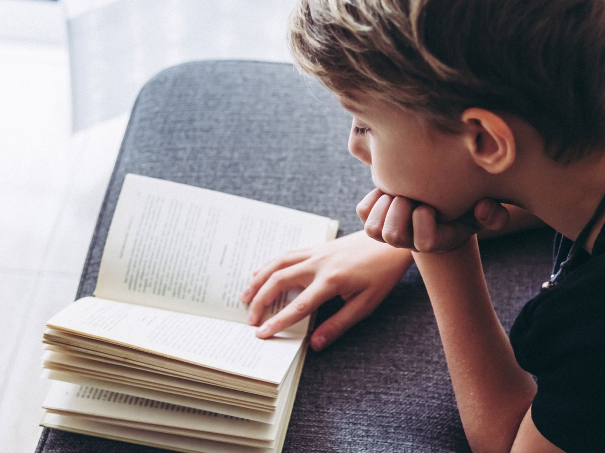 Junge, ca. 10 Jahre alt, liegt auf der Couch und liest ein Buch.