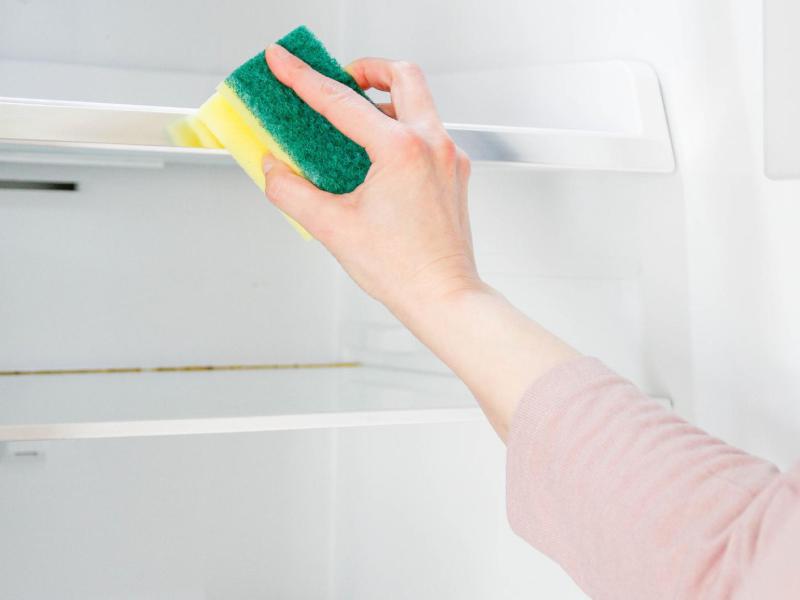 Frau wischt den Kühlschrank mit einem Schwamm.