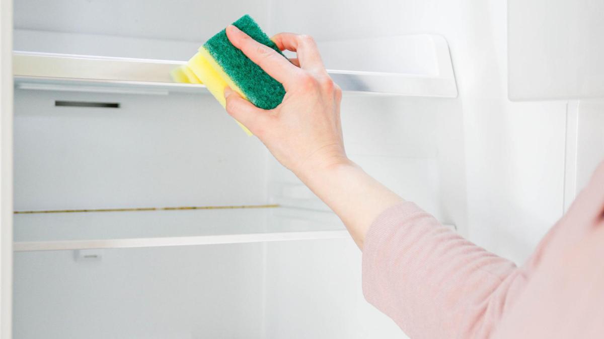 Frau wischt den Kühlschrank mit einem Schwamm.