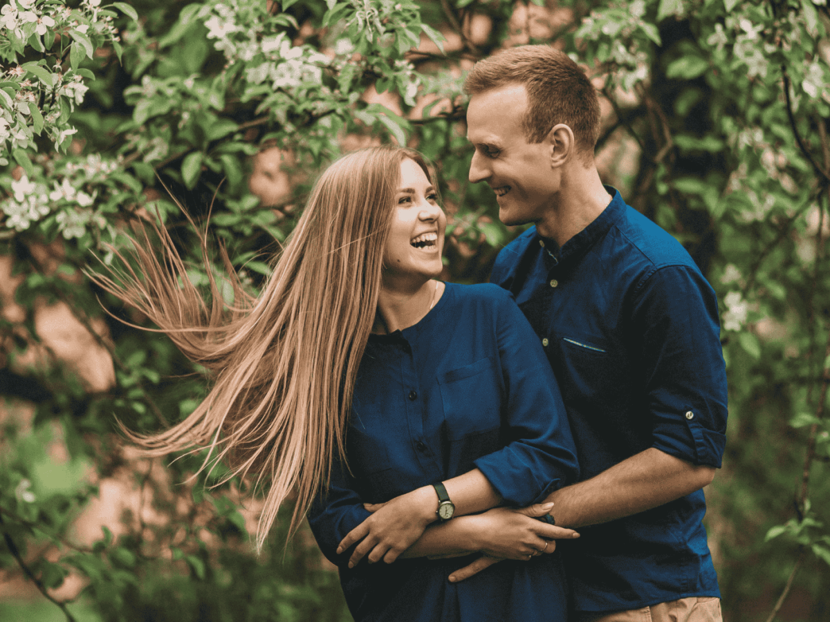 Frau und Mann vor einem blühenden Baum lachen und halten sich in den Armen