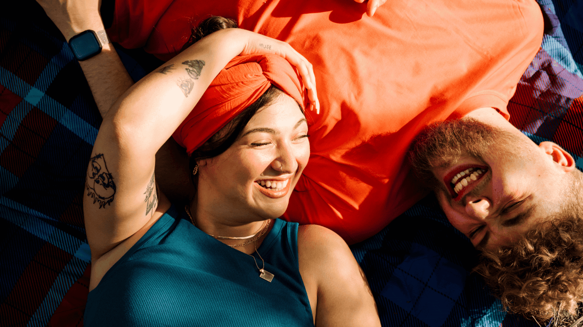 Frau mit orangenem Turban liegt lachend auf der Brust eines Mannes mit orangenem T-Shirt