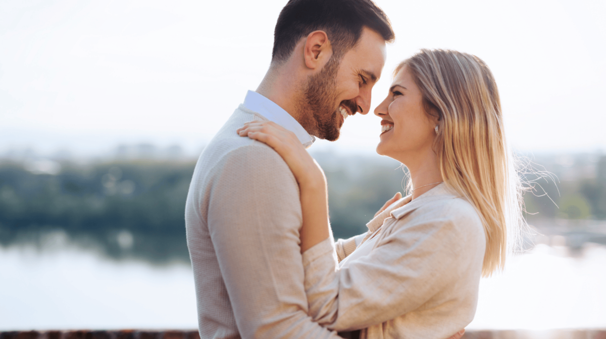 Frau und Mann stehen sich am Wasser gegenüber und schauen sich lächelnd in die Augen
