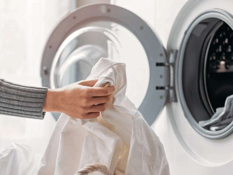 Person räumt weißes Kleidungsstück in die Waschmaschine