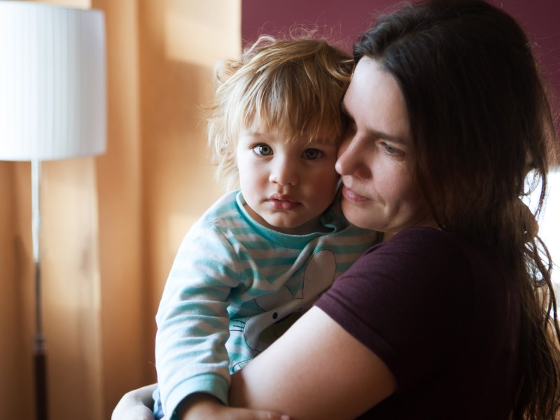 Mutter trägt trauriges Kind auf dem Arm.