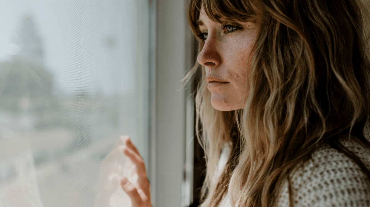 Junge Frau schaut traurig aus dem Fenster.