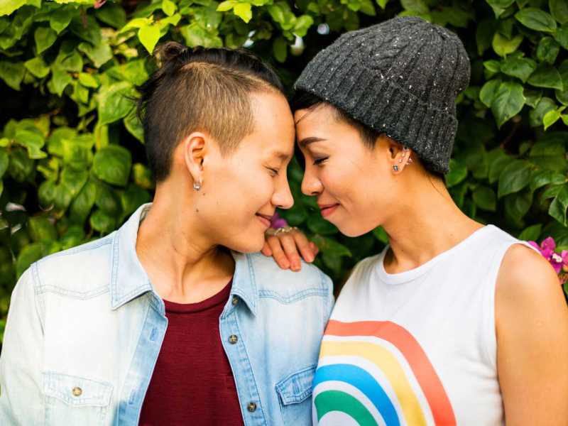 Junges, lesbisches Pärchen steht Stirn an Stirn zusammen und lächelt sich an.