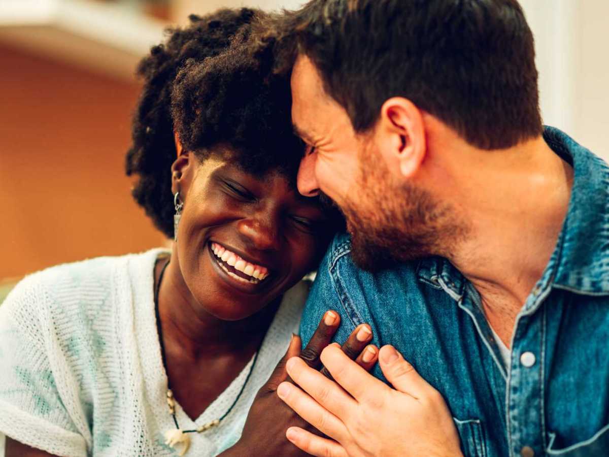 Frau schmiegt sich verliebt an ihren Partner. Beide lächeln.