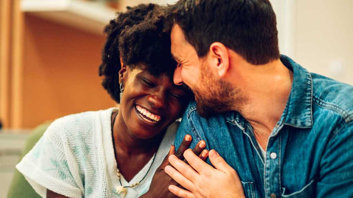 Frau schmiegt sich verliebt an ihren Partner. Beide lächeln.