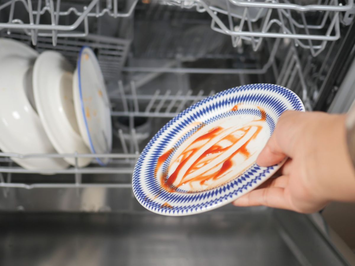 Hand räumt dreckigen Teller in Spülmaschine