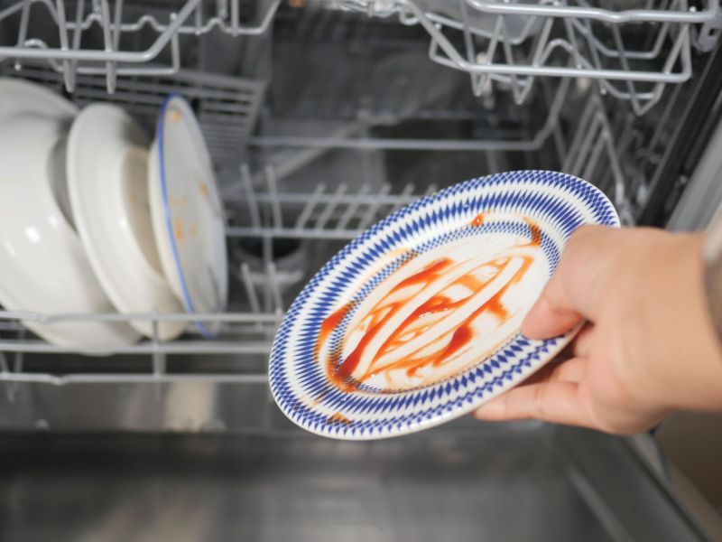 Hand räumt dreckigen Teller in Spülmaschine